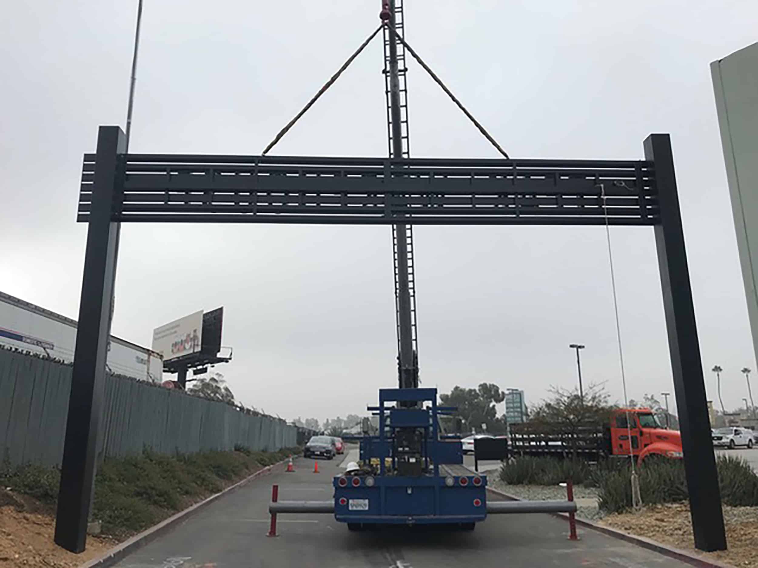 An example where Signs for San Diego used a crane to install a roadway arch, which allowed installers to get the poles up and inground, and to lift the arch itself up to be bolted in with a bucket truck.
